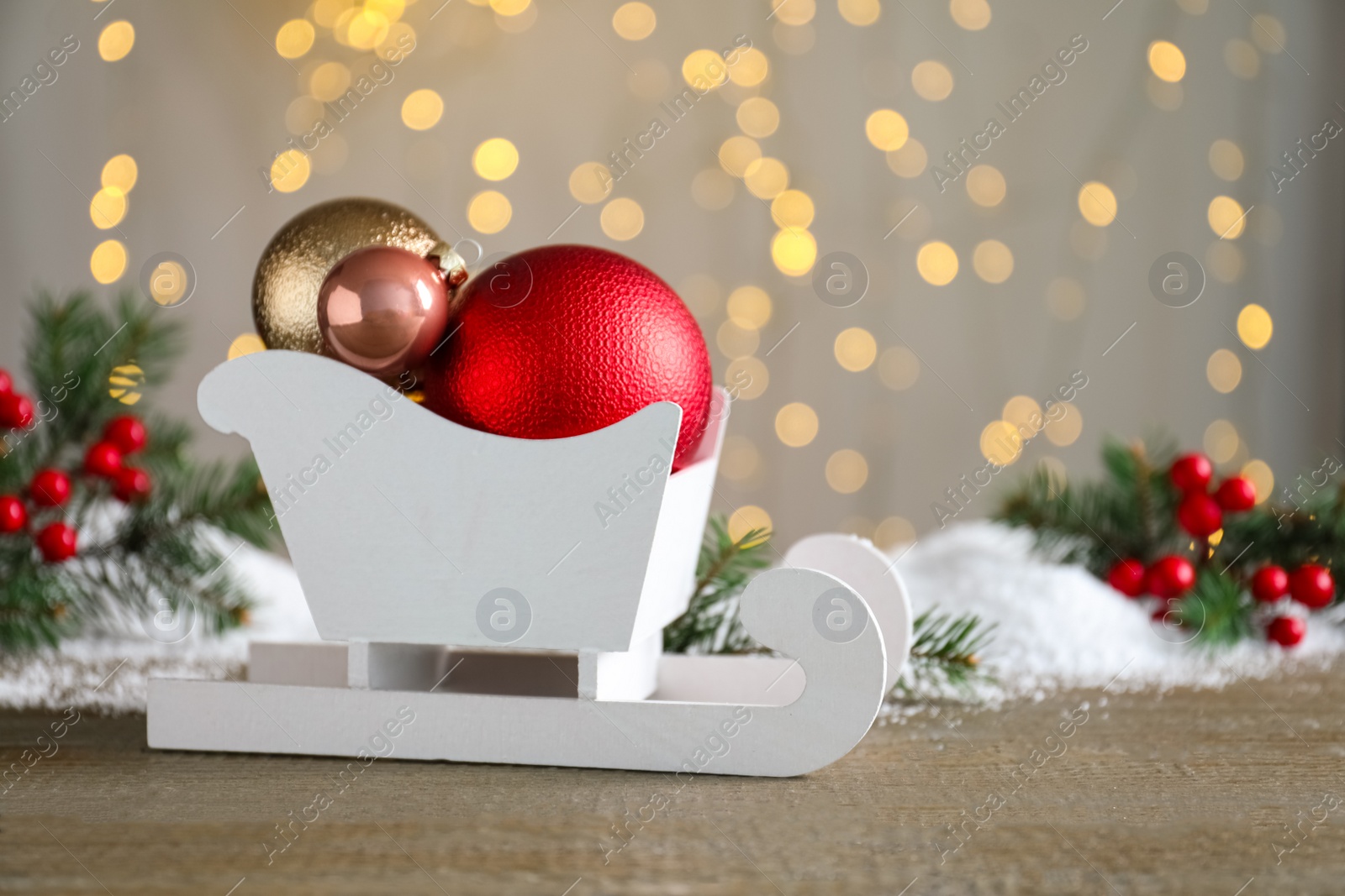 Photo of Sleigh with Christmas decorations on wooden table against blurred lights