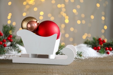 Sleigh with Christmas decorations on wooden table against blurred lights