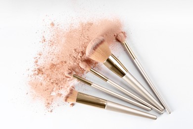 Photo of Makeup brushes and scattered face powder on white background, flat lay