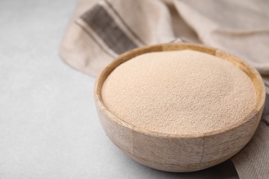 Photo of Granulated yeast in wooden bowl on light gray table, closeup. Space for text