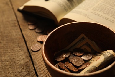 Donate and give concept. Bowl with coins, dollar banknotes and Bible on wooden table, closeup. Space for text