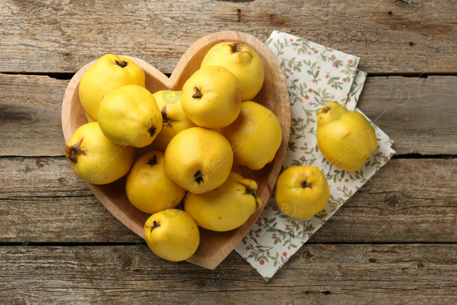 Photo of Tasty ripe quinces in heart shaped bowl on wooden table, top view