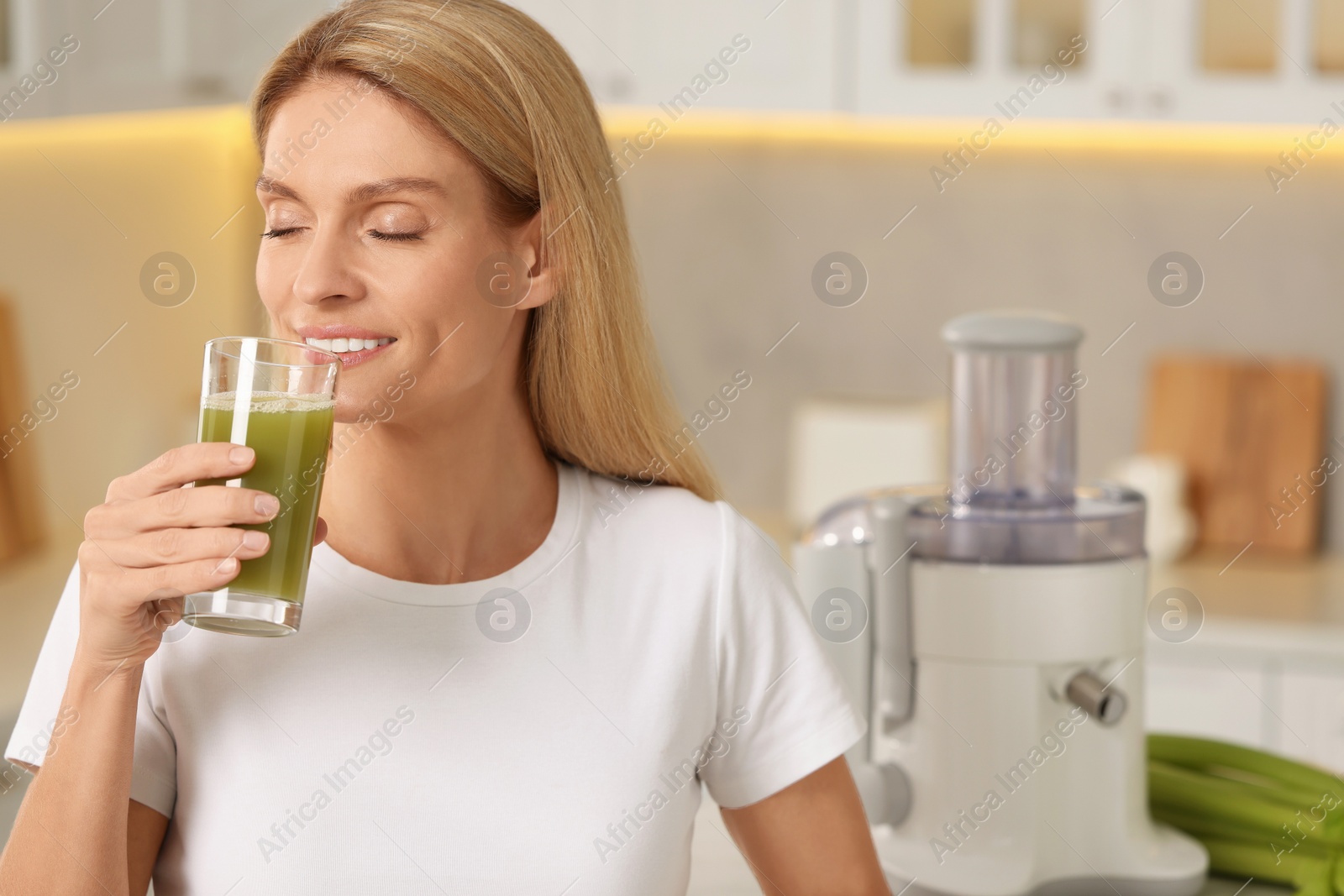 Photo of Woman drinking fresh celery juice in kitchen. Space for text