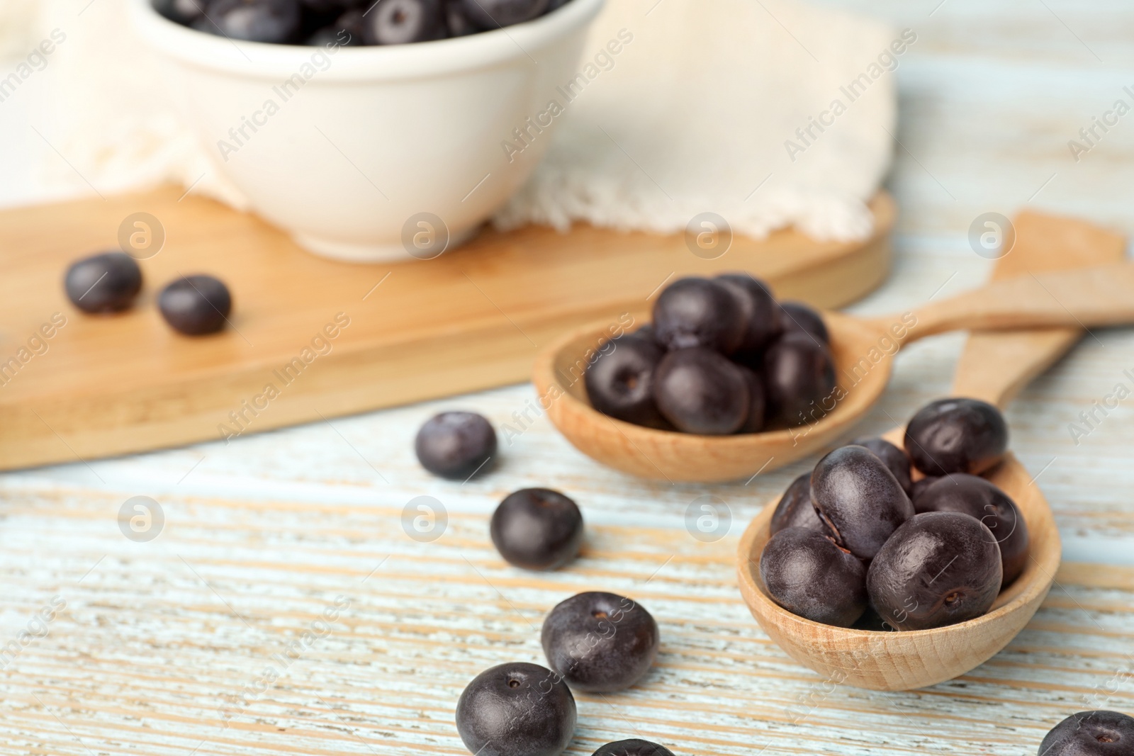 Photo of Spoons of fresh acai berries on light wooden table, closeup. Space for text