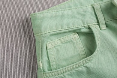 Photo of Stylish light green jeans on grey fabric, closeup of inset pocket