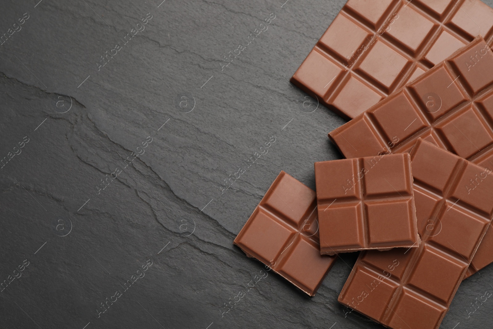 Photo of Delicious milk chocolate on black table, flat lay. Space for text