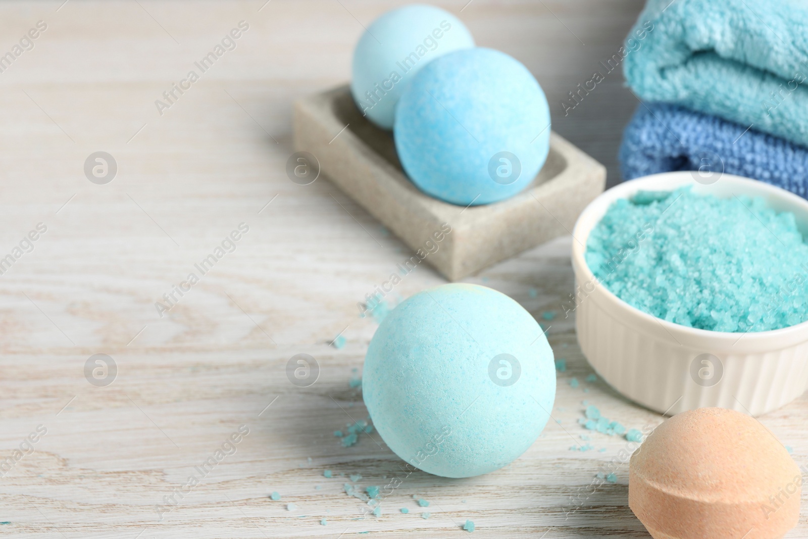 Photo of Beautiful aromatic bath bombs and sea salt on light wooden table. Space for text