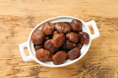 Photo of Roasted edible sweet chestnuts in dish on light wooden table, top view