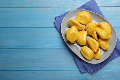 Delicious exotic jackfruit bulbs on light blue wooden table, flat lay. Space for text