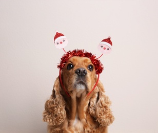Photo of Adorable Cocker Spaniel dog in Santa headband on light background