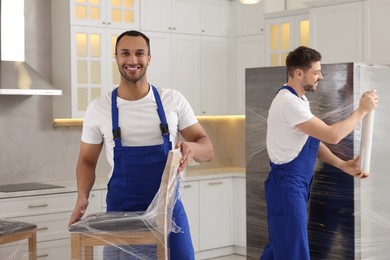 Photo of Male movers with chairs and refrigerator in new house