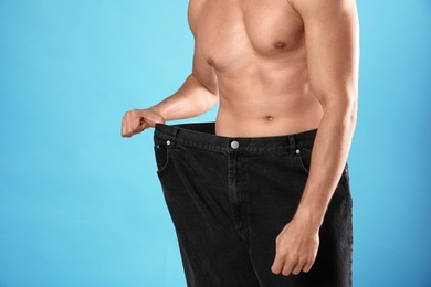 Photo of Young man with slim body in old big size jeans on light blue background, closeup view. Space for text