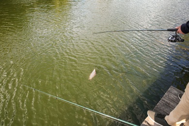 Man with rod fishing on wooden pier at riverside. Recreational activity