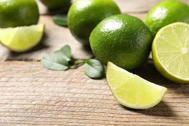 Photo of Whole and cut fresh limes on wooden table. Space for text