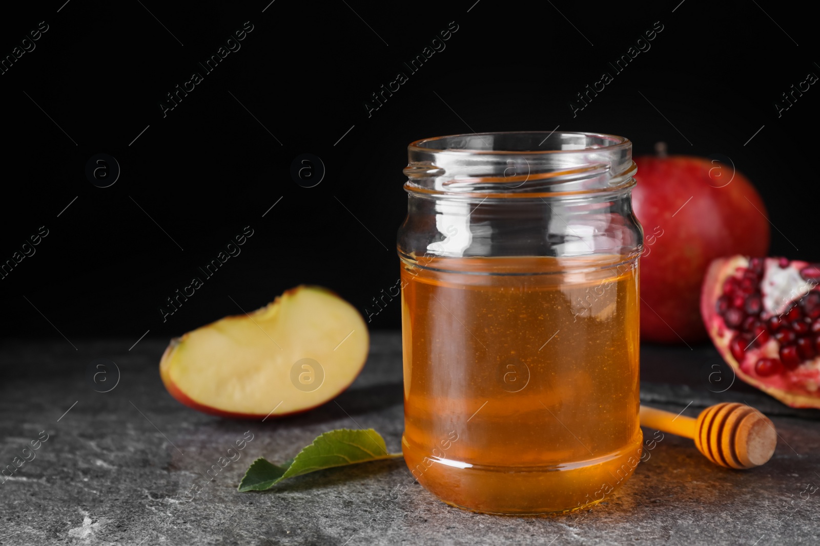 Photo of Honey near pomegranate and apple on grey table. Rosh Hashanah holiday