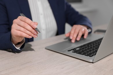 Woman with pen working on laptop at wooden table, closeup. Electronic document management