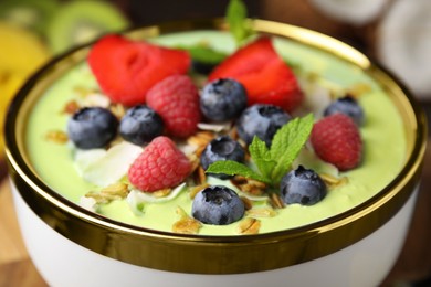 Photo of Tasty matcha smoothie bowl served with berries and oatmeal on table, closeup. Healthy breakfast