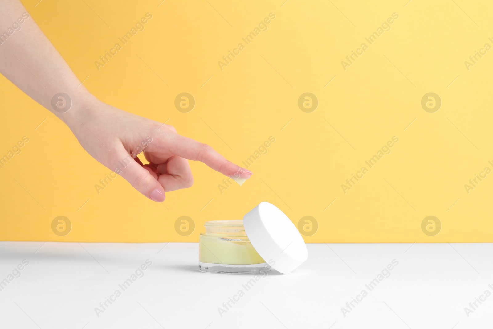 Photo of Woman with jar of cream on yellow background, closeup