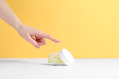 Woman with jar of cream on yellow background, closeup