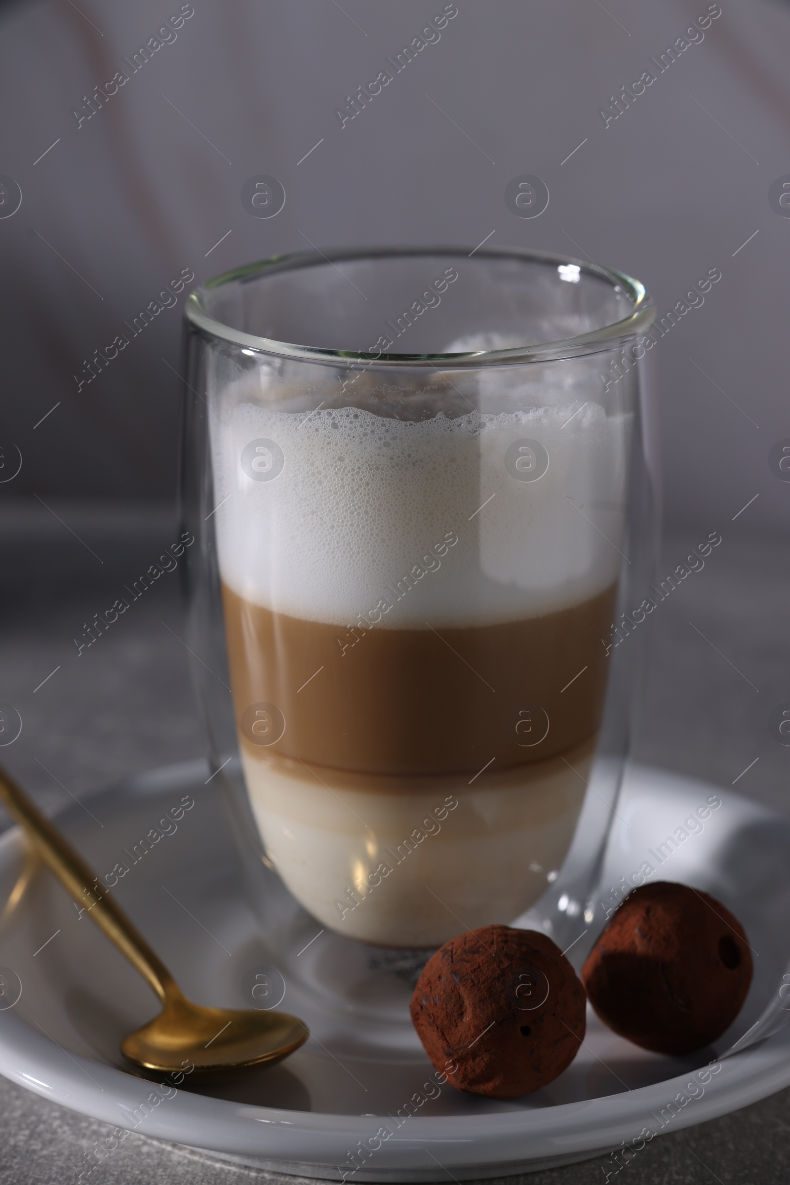 Photo of Aromatic latte macchiato in glass and chocolate candies on grey table, closeup