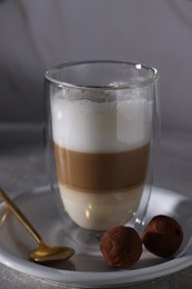 Photo of Aromatic latte macchiato in glass and chocolate candies on grey table, closeup