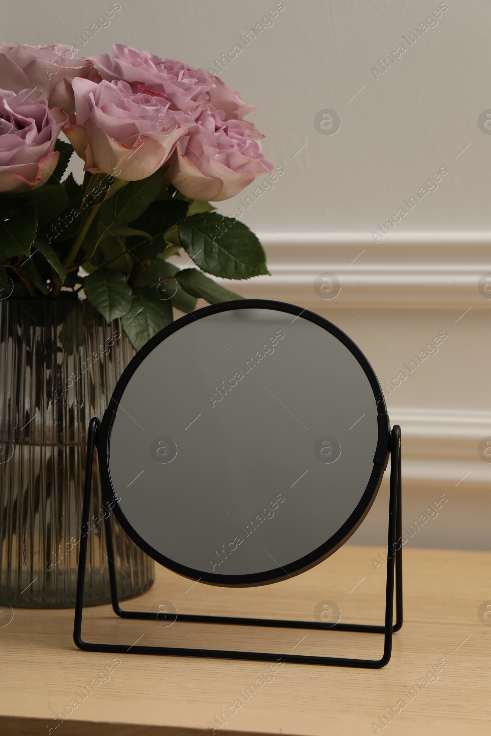 Photo of Mirror and vase with pink roses on wooden dressing table, closeup