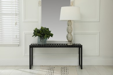 Photo of Console table with lamp, bouquet of green branches and mirror in room. Interior design