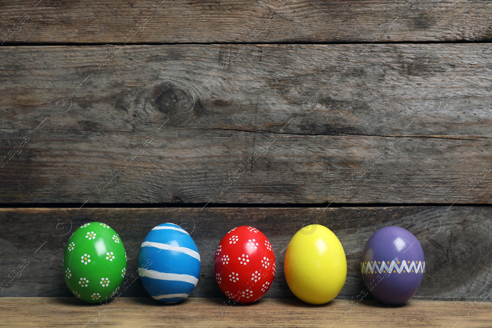 Photo of Decorated Easter eggs on table near wooden wall. Space for text