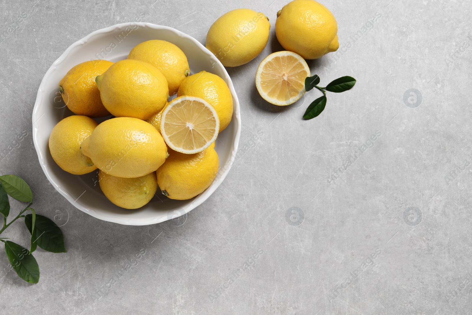 Photo of Fresh lemons and green leaves on grey table, top view. Space for text