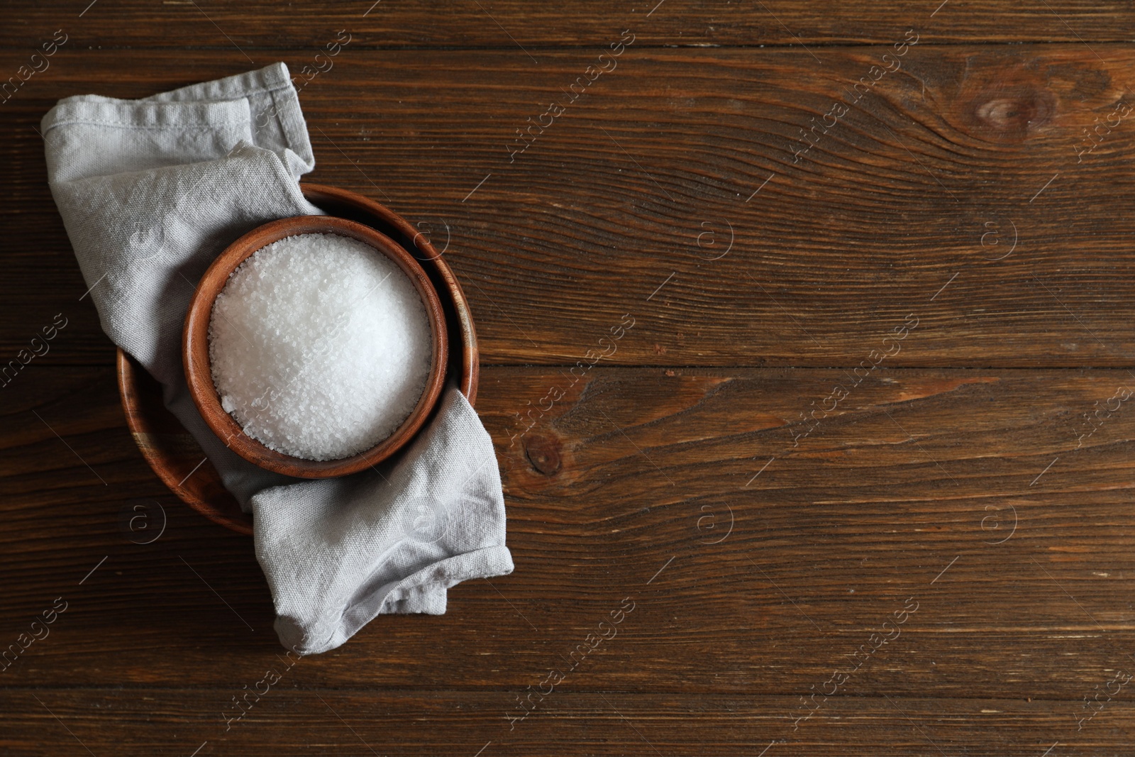 Photo of Organic salt in bowl on wooden table, top view. Space for text