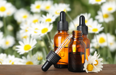 Bottles of essential oil and chamomile flowers on wooden table against blurred background. Space for text