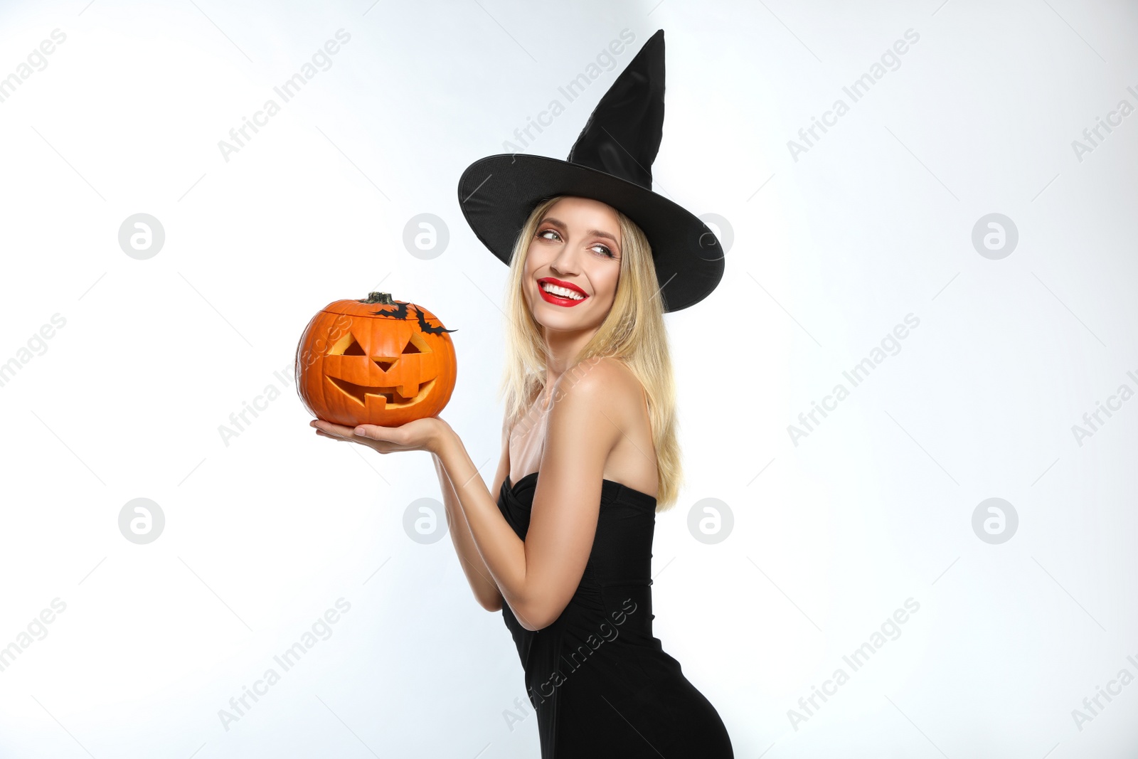 Photo of Beautiful woman in witch costume with jack o'lantern on white background. Halloween party