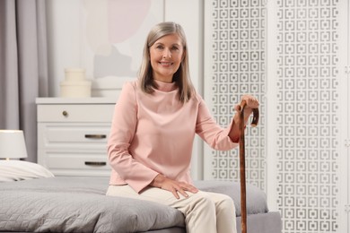 Mature woman with walking cane on bed at home