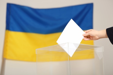 Woman putting voting paper into ballot box against Ukrainian flag, closeup. Space for text