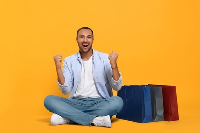 Photo of Happy African American man with shopping bags on orange background