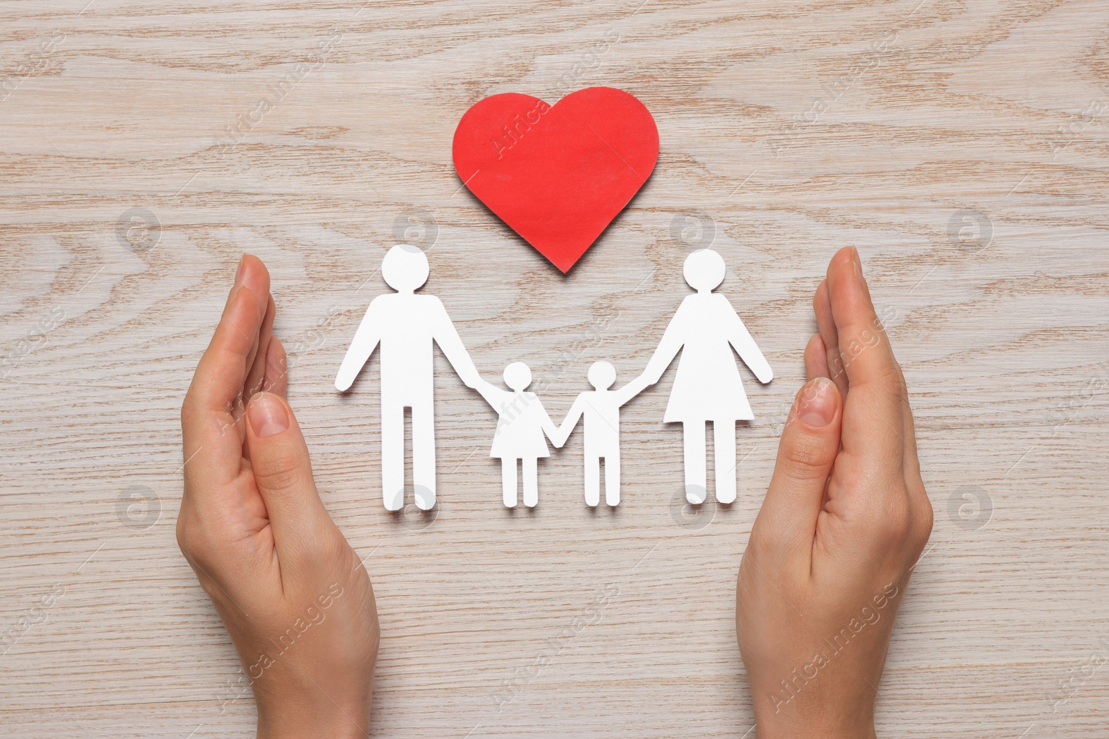 Photo of Woman protecting paper family cutout at white wooden table, top view. Insurance concept