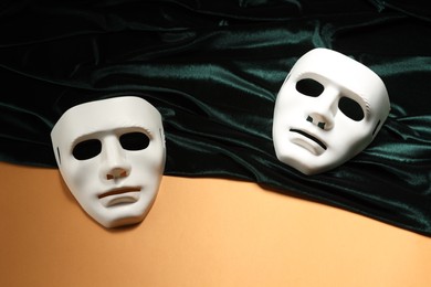 Theater arts. White masks and green fabric on pale orange background, above view