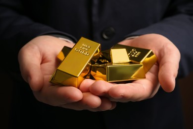 Photo of Man holding many shiny gold bars, closeup