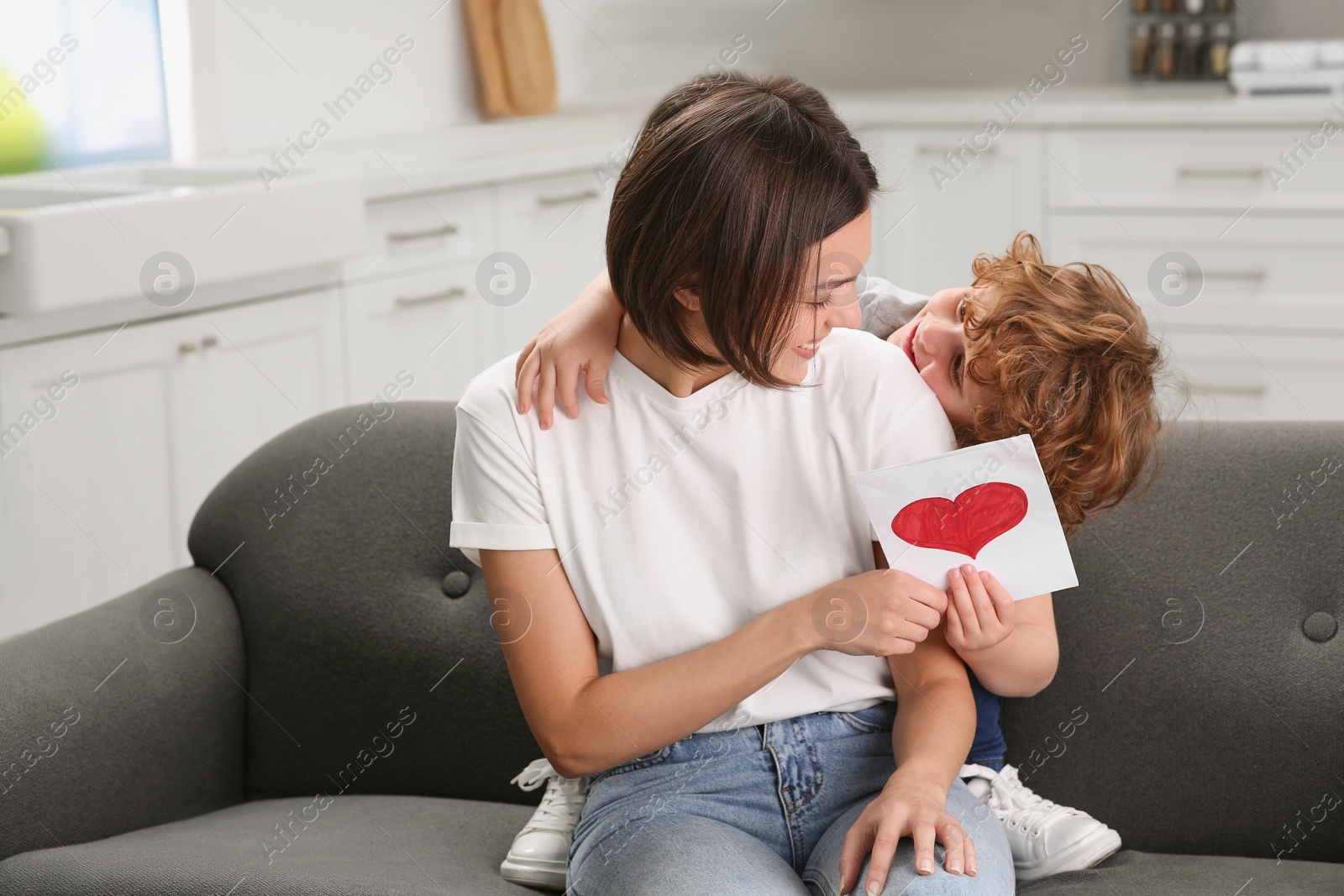 Photo of Little son congratulating his mom with Mother`s day at home. Woman holding greeting card