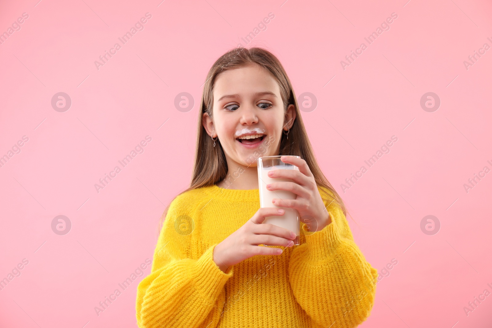 Photo of Happy little girl with milk mustache holding glass of tasty dairy drink on pink background