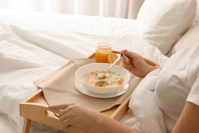 Photo of Sick woman eating fresh homemade soup to cure flu in bed at home, closeup