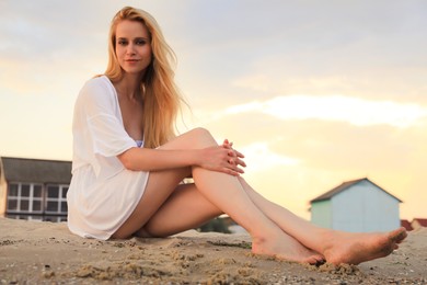 Photo of Beautiful young woman sitting on beach at sunset