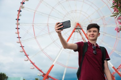 Photo of Teenage boy taking selfie near Ferris wheel outdoors. Space for text