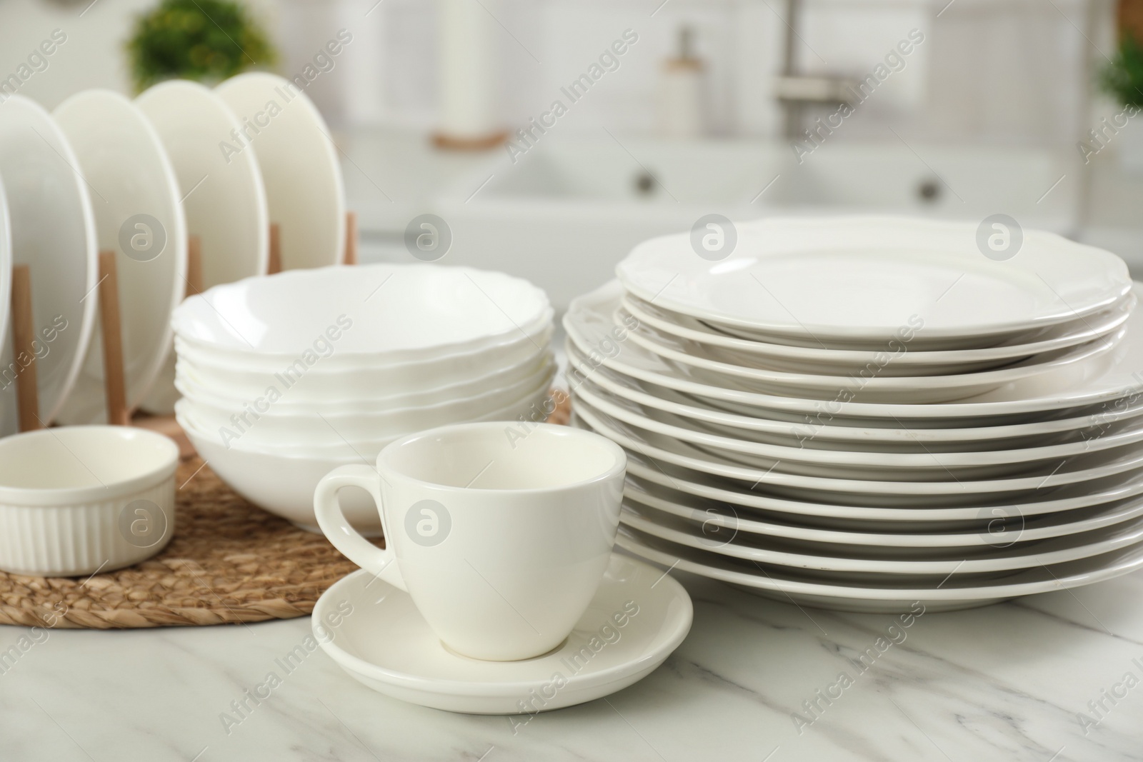 Photo of Clean plates, bowls and cup on white marble table in kitchen