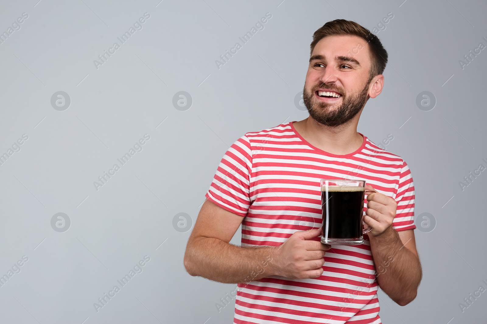 Photo of Handsome man with cold kvass on light grey background. Traditional Russian summer drink