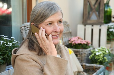 Photo of Beautiful senior woman sitting and talking on smartphone outdoors, space for text
