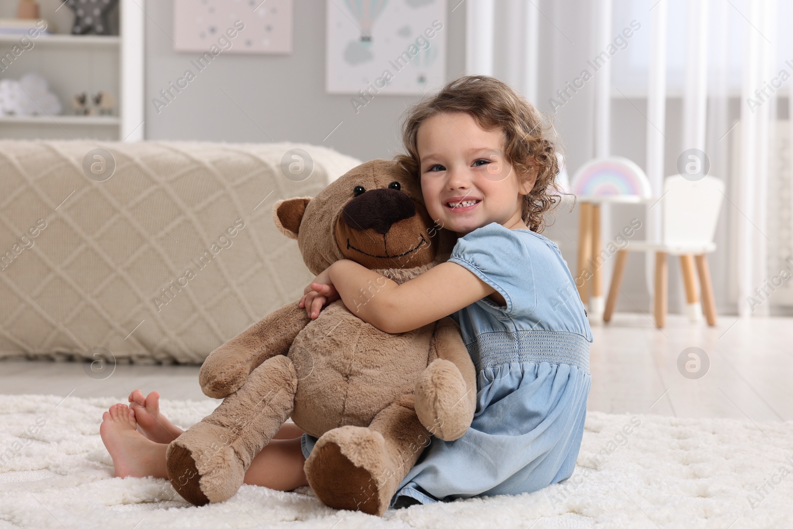 Photo of Cute little girl with teddy bear on floor at home