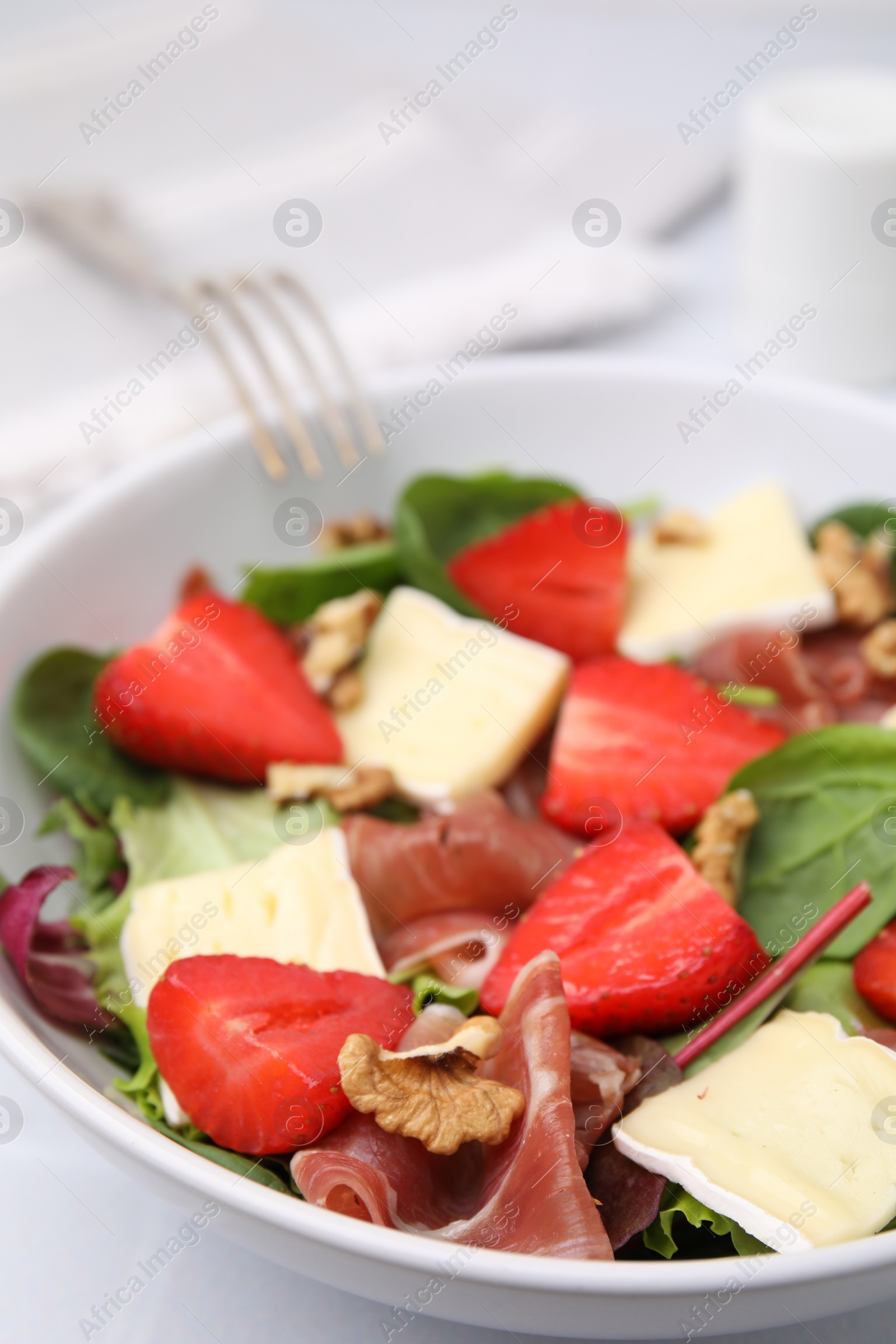 Photo of Tasty salad with brie cheese, prosciutto, strawberries and walnuts on table, closeup