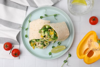 Delicious sandwich wraps with fresh vegetables, bell pepper, tomatoes and slice of lime on white tiled table, flat lay