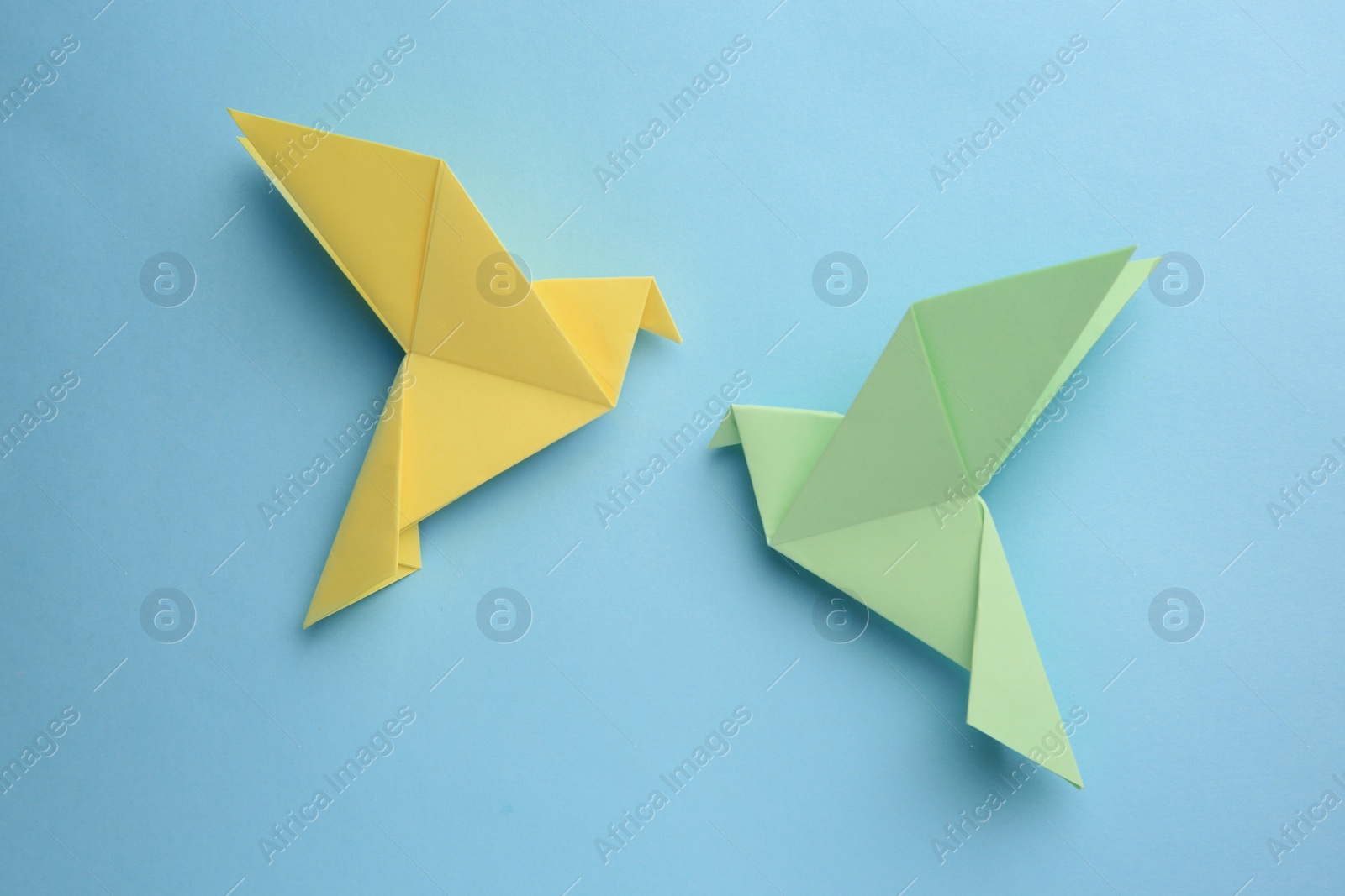 Photo of Origami art. Colorful handmade paper birds on light blue background, flat lay